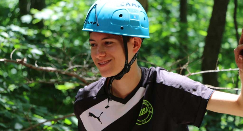 A person wearing a helmet smiles amongst a wooded area. 